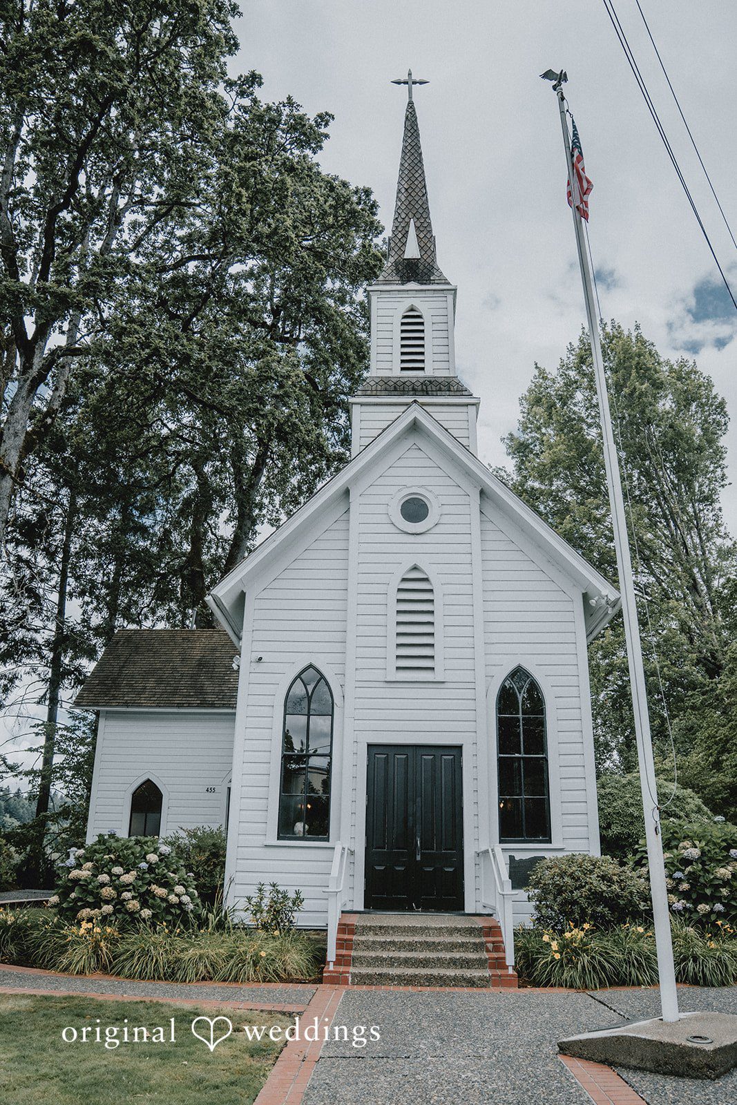 Ashley + Forrest A historic white church with a tall steeple stands surrounded by green trees.