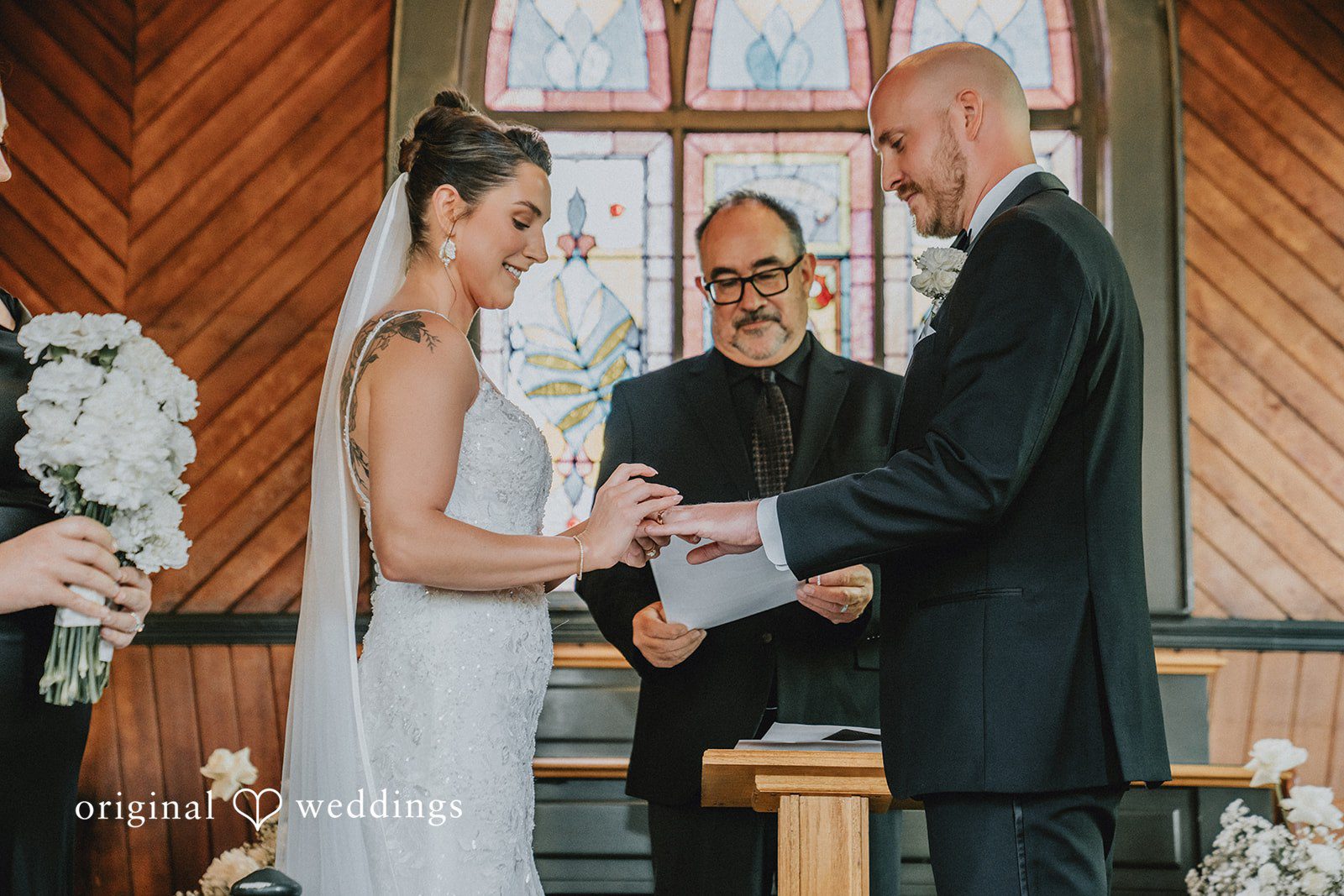 Ashley + Forrest A bride and groom exchange vows at the altar with an officiant standing between them.
