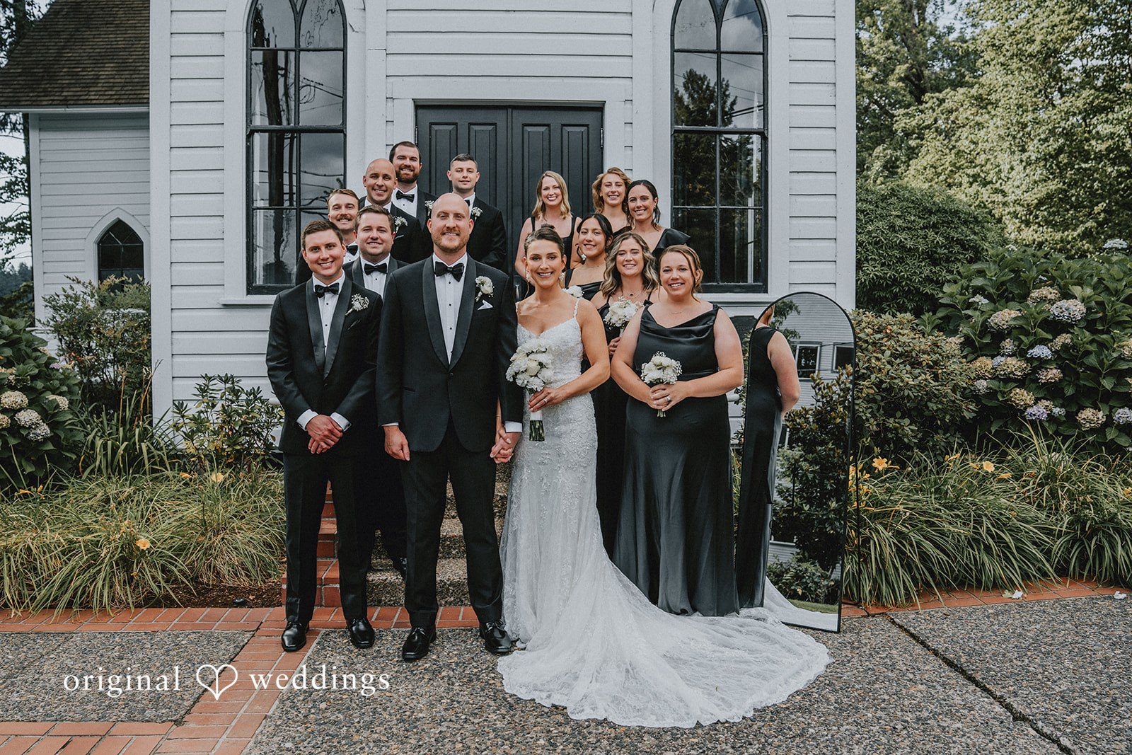 Ashley + Forrest A wedding party in formal attire poses together standing in front of a white building.