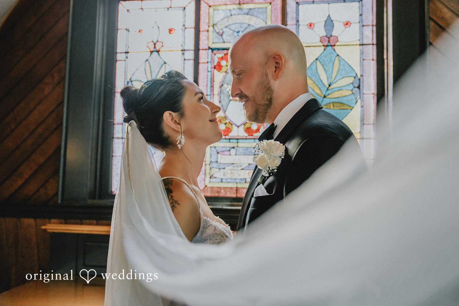 Ashley + Forrest A close-up view of a bride and groom embracing as a sheer white veil frames them.