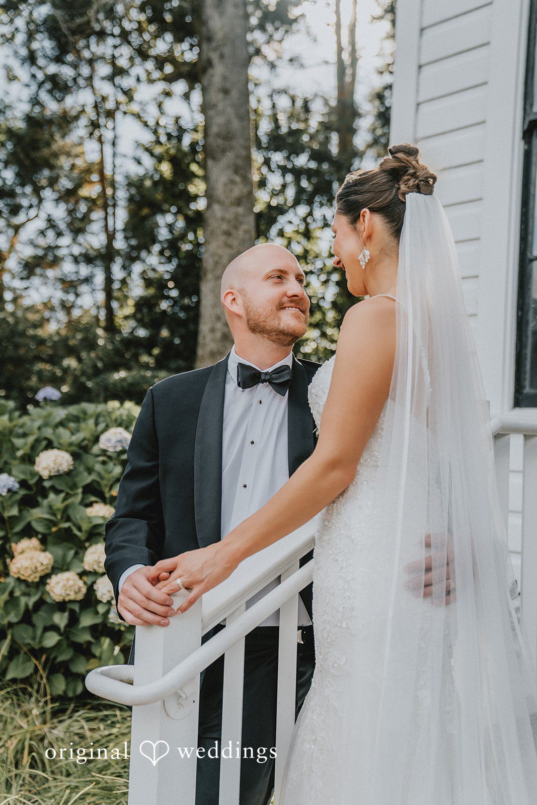 Ashley + Forrest A bride and groom smile at each other while posing on a white staircase.