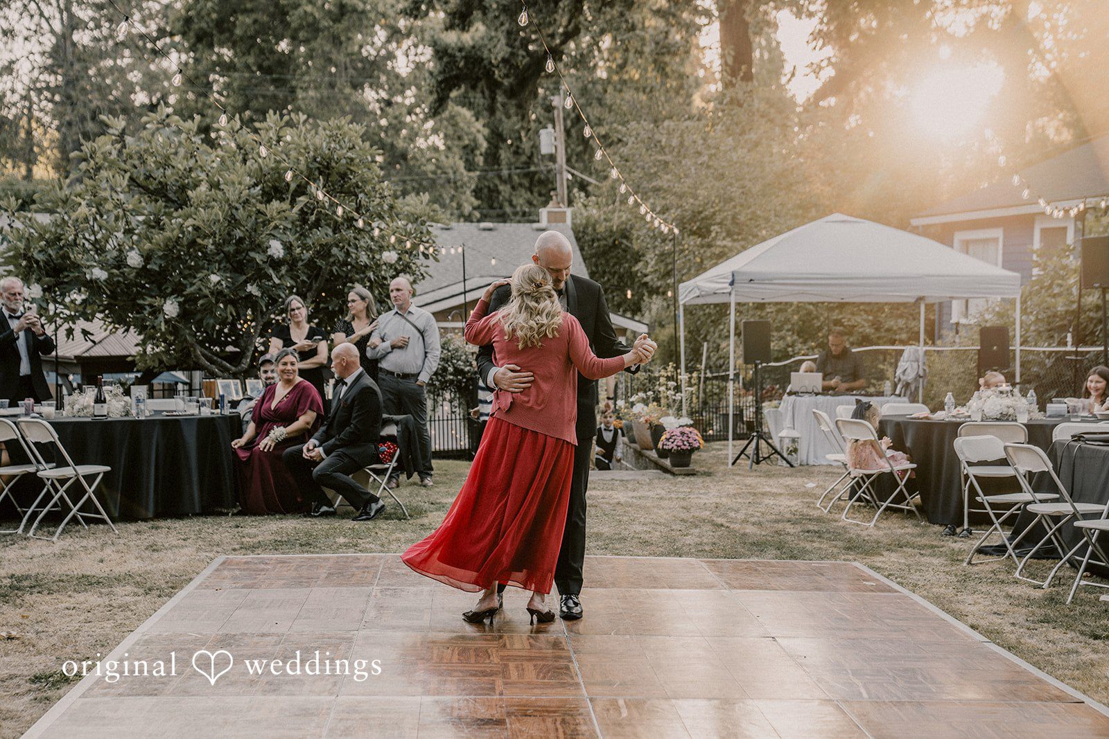 Ashley + Forrest A woman in a red dress dances on a wooden floor with wedding reception guests in the background.