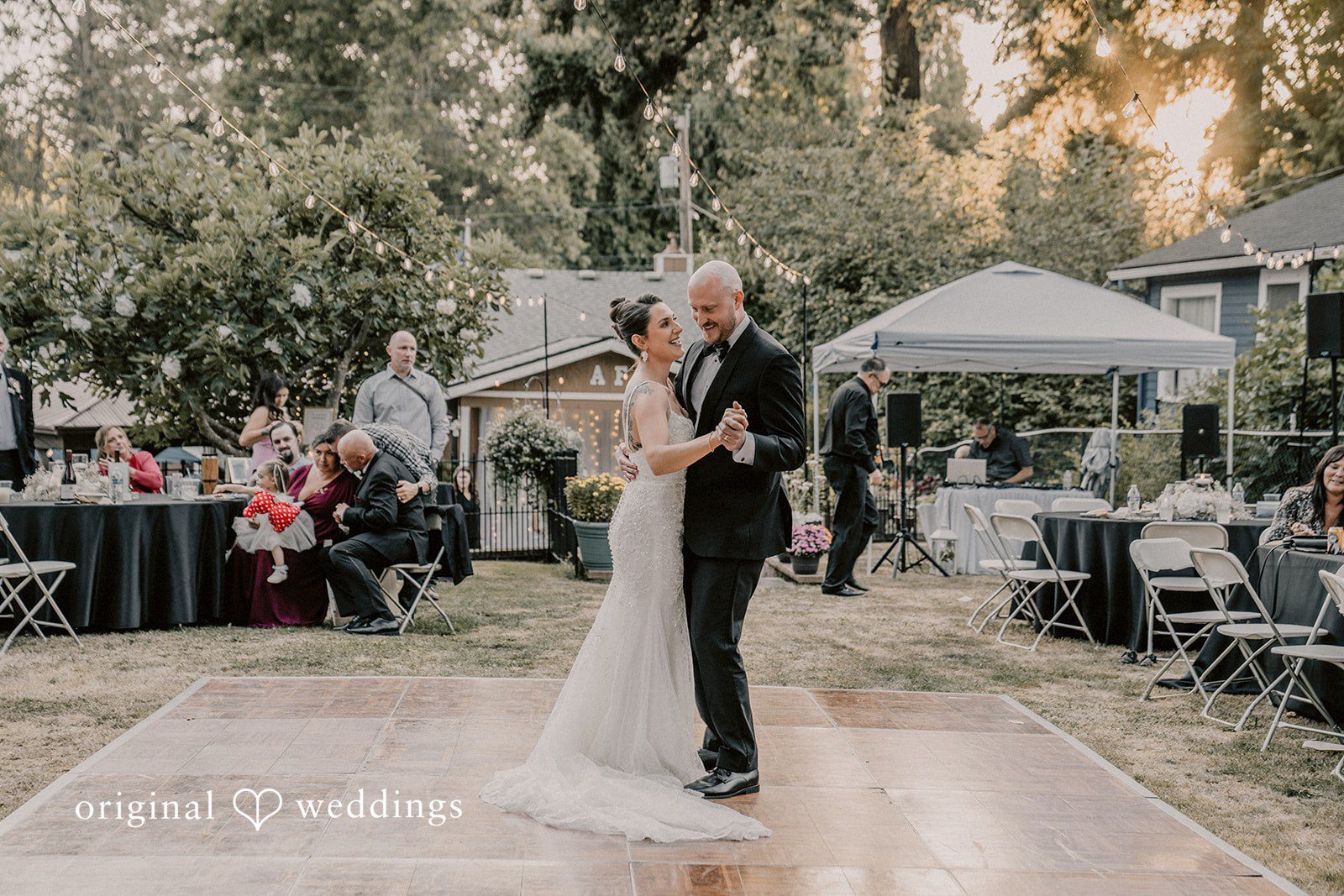 Ashley + Forrest A bride and groom share a slow dance on an open wooden floor under the trees.