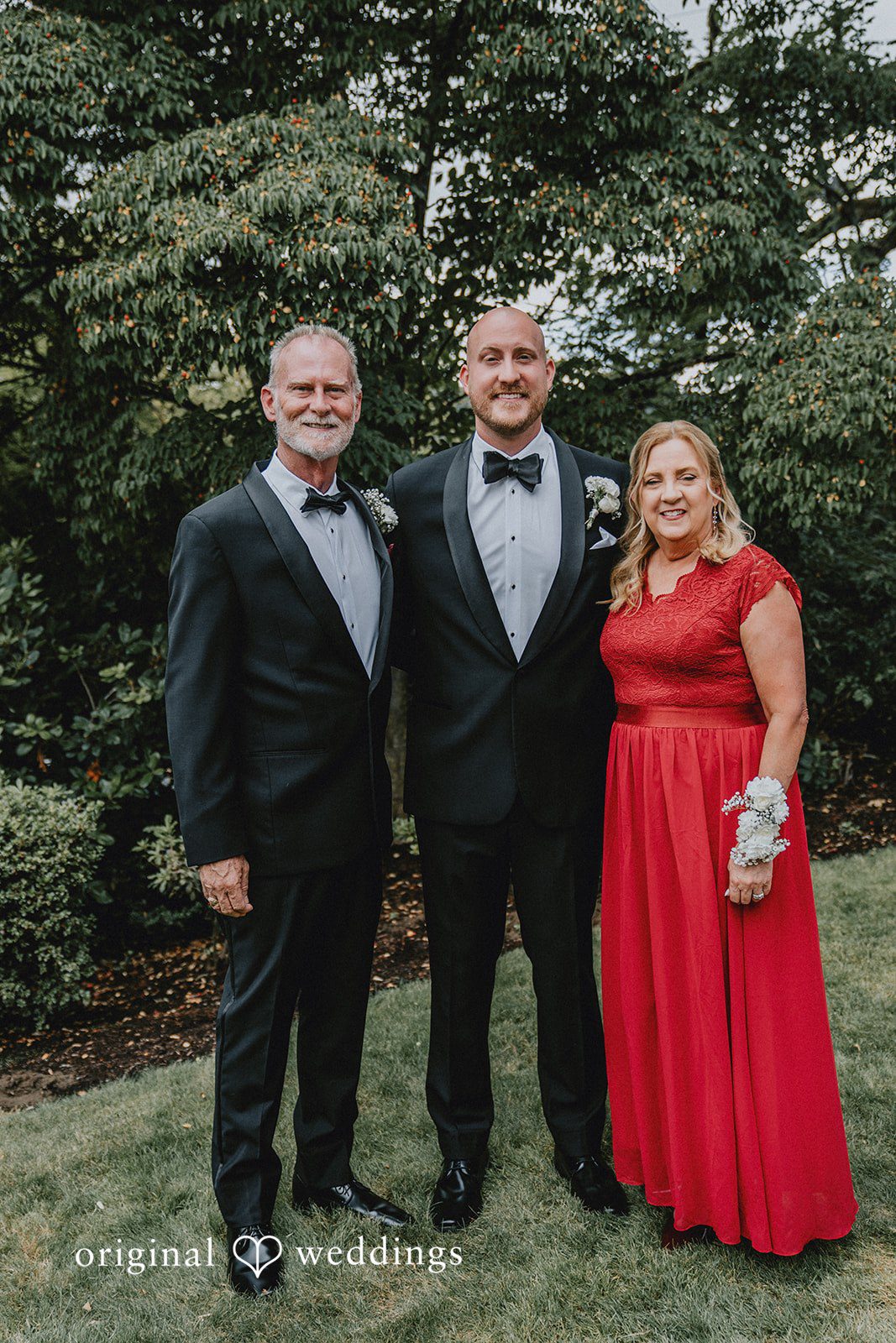 Ashley + Forrest A man and groom in formal wear pose standing next to another woman in a bright red dress.