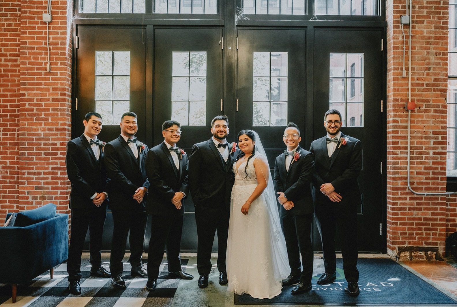 Bride with her groomsmen at the barn doors, captured by Providence wedding photographers from Original Weddings at The Barn at Blackstone National