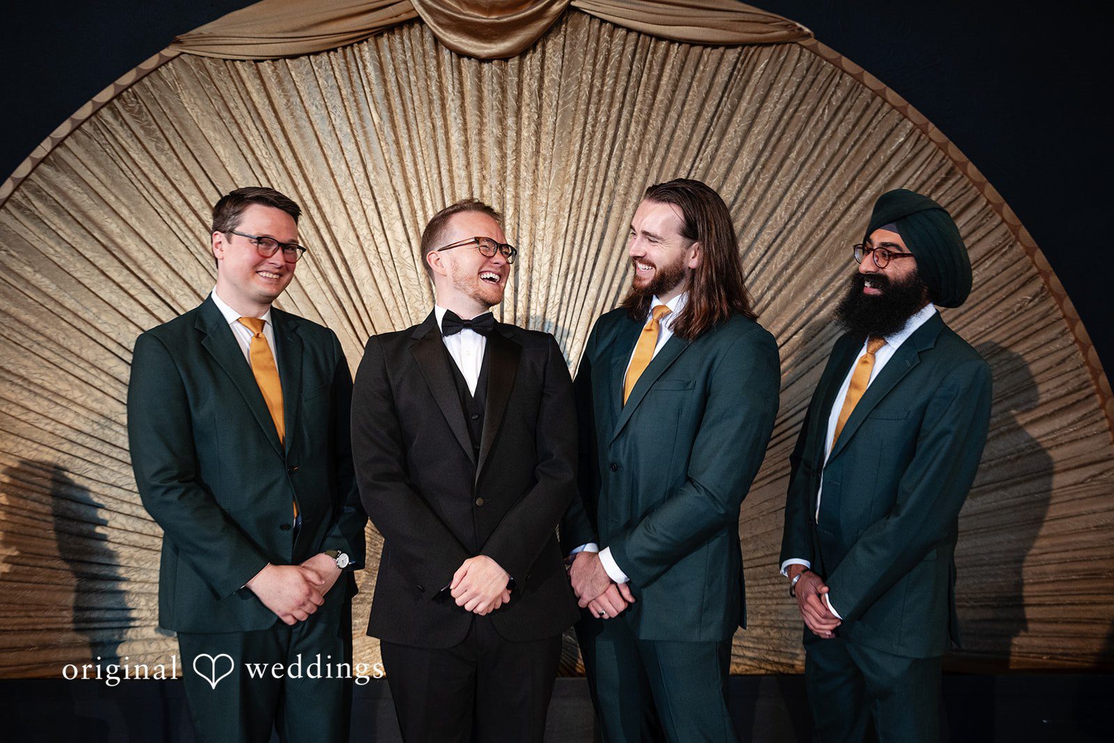 Groomsmen standing by the gold fan backdrop during the ceremony