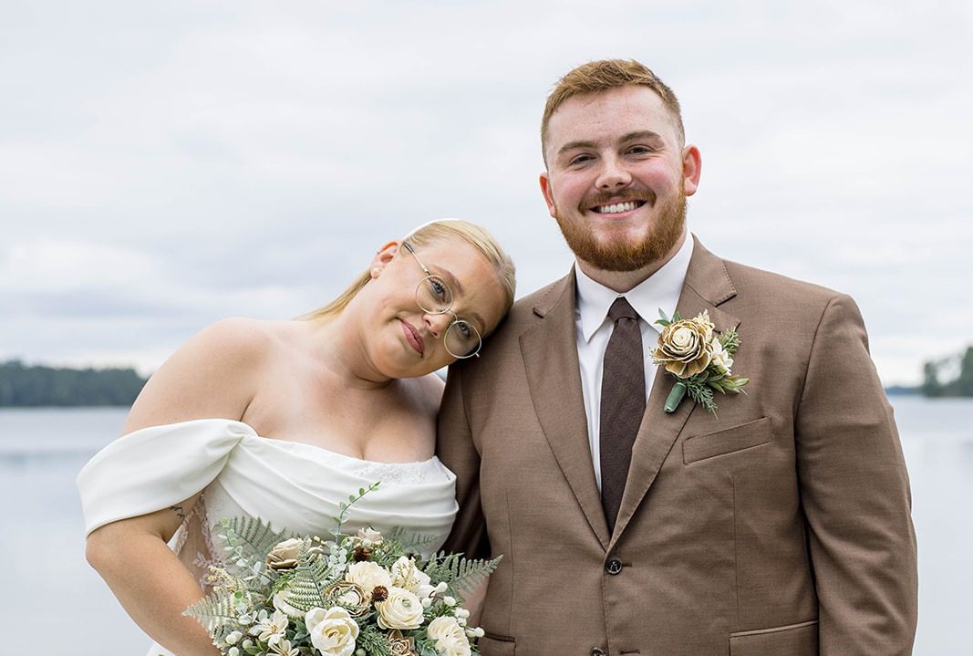 Anna and Justin smiling together by Pleasant Lake, captured by Minneapolis wedding photographers from Original Weddings at Spirit in the Pines