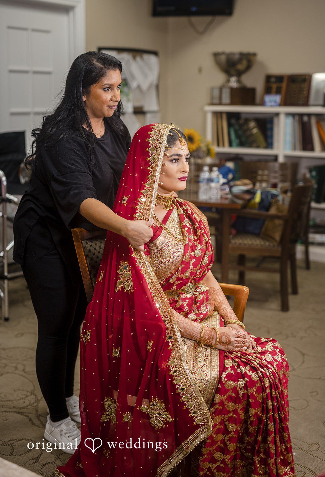 Nicholas + Nisha Bride in a red lehenga receiving final adjustments to her bridal look from a stylist.