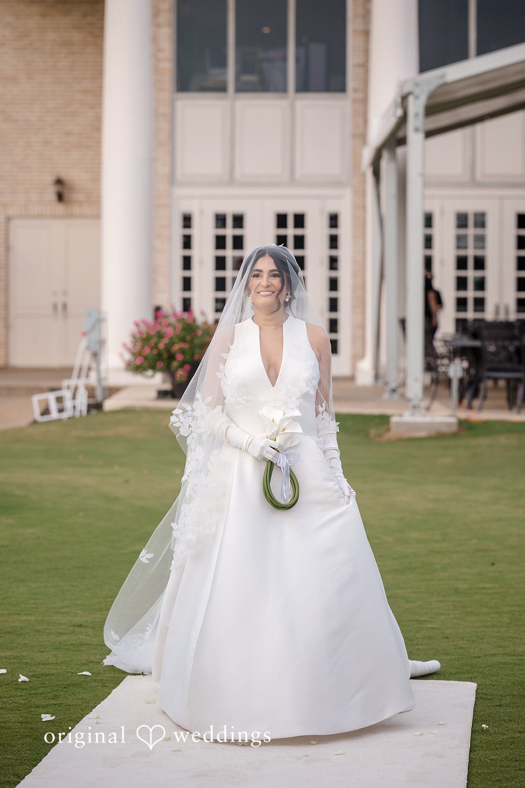 Nicholas + Nisha Bride posing in her white wedding dress on a grassy field.