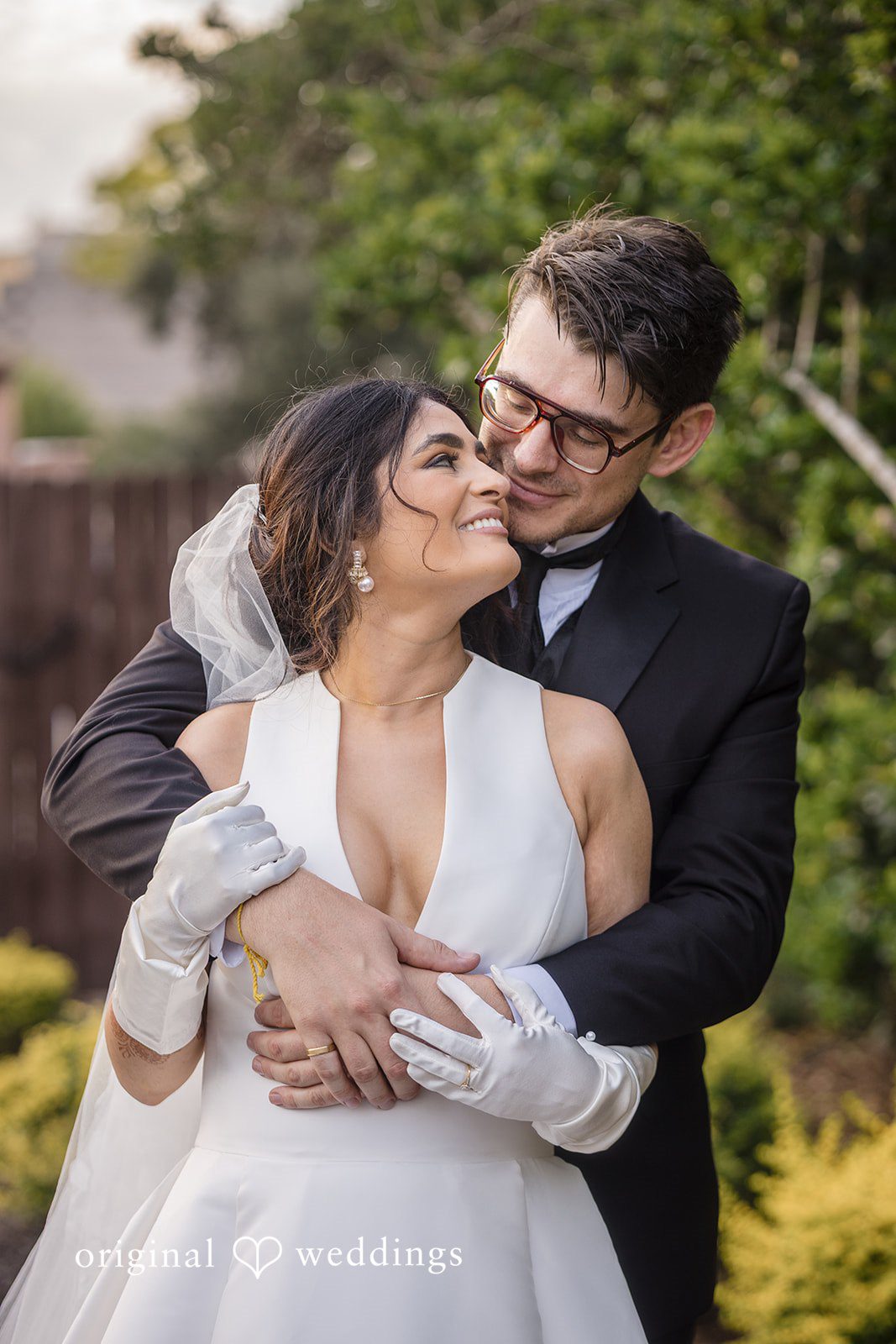 Nicholas + Nisha Groom embracing the bride from behind while she smiles.