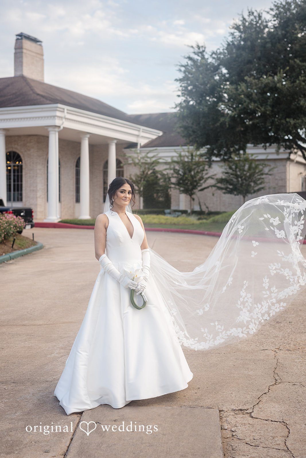 Nicholas + Nisha Bride walking across a lawn with her long veil flowing behind her.