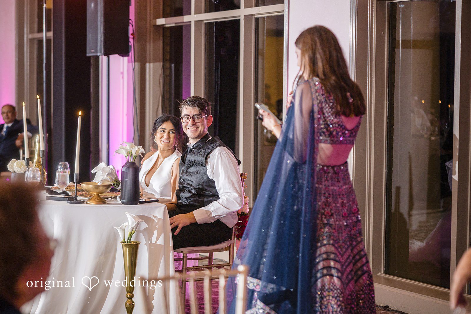Nicholas + Nisha Guests in formal attire gathered around a table at a wedding reception.
