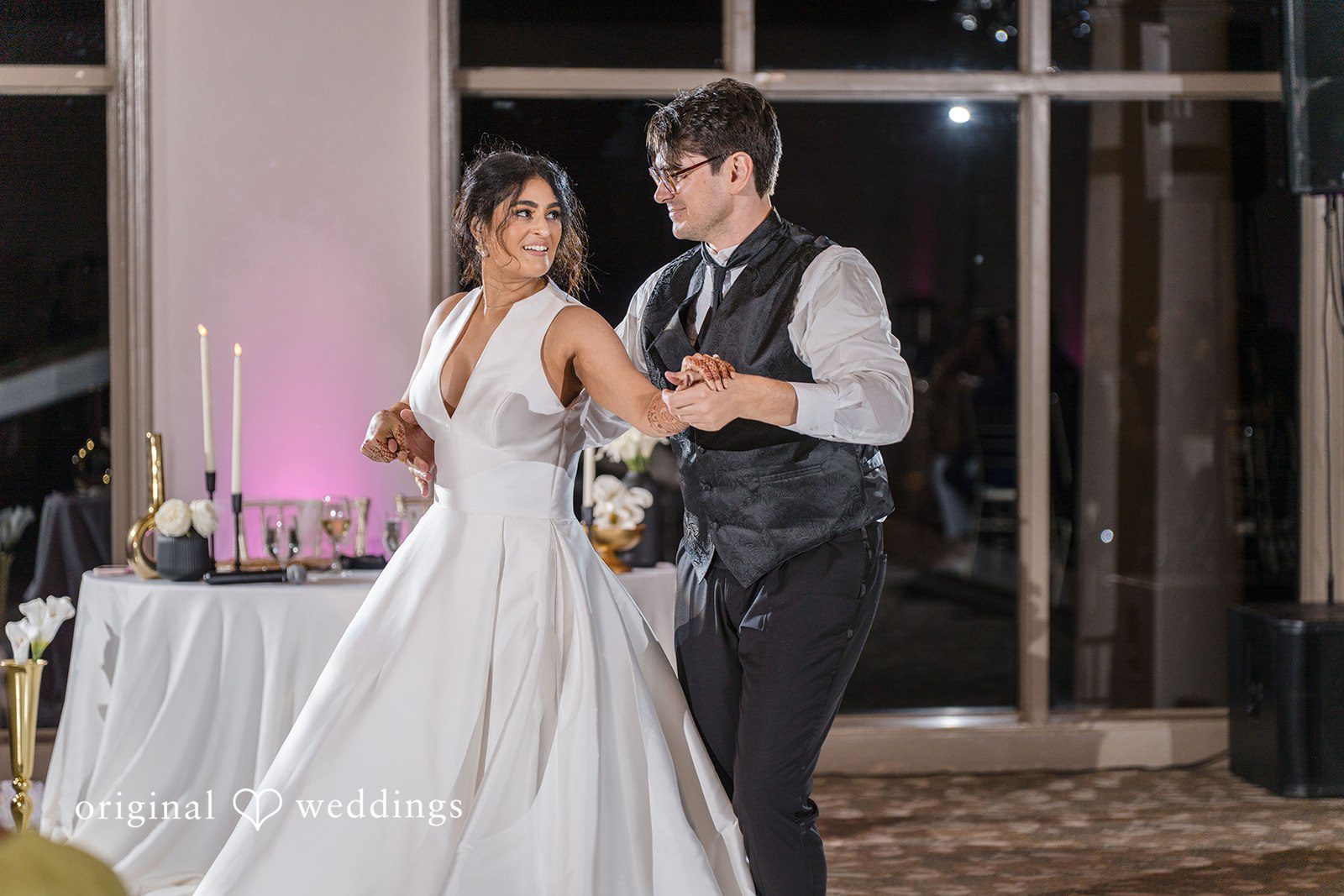 Nicholas + Nisha Bride and groom standing near a reception table while interacting.