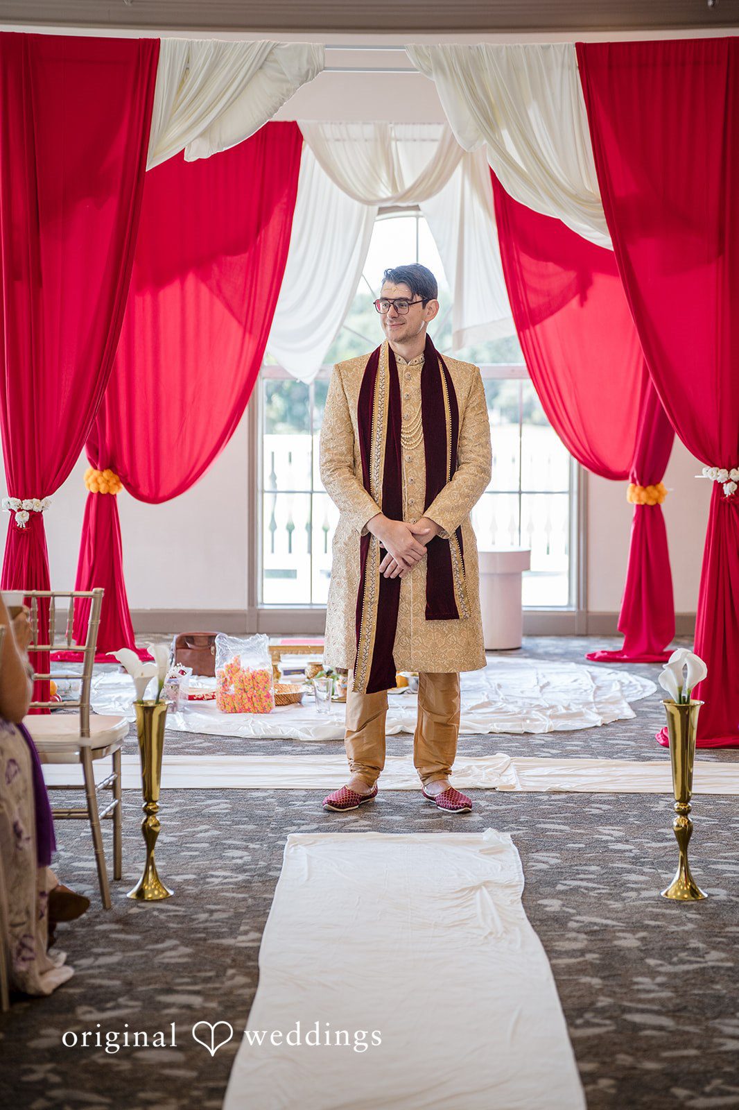 Nicholas + Nisha Groom standing under a red draped canopy during a wedding ceremony.