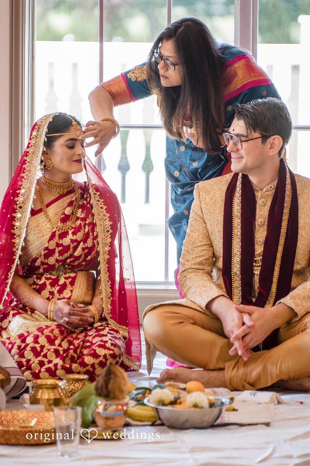 Nicholas + Nisha Individuals interacting during a traditional wedding ceremony under bright lighting.