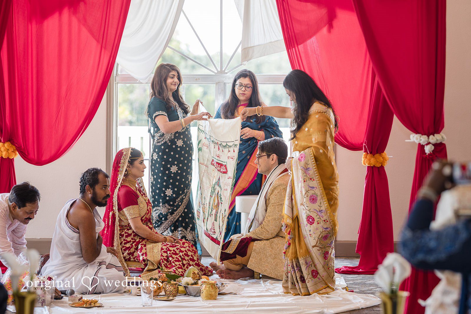 Nicholas + Nisha Guests dressed in formal attire standing near vibrant red drapery.