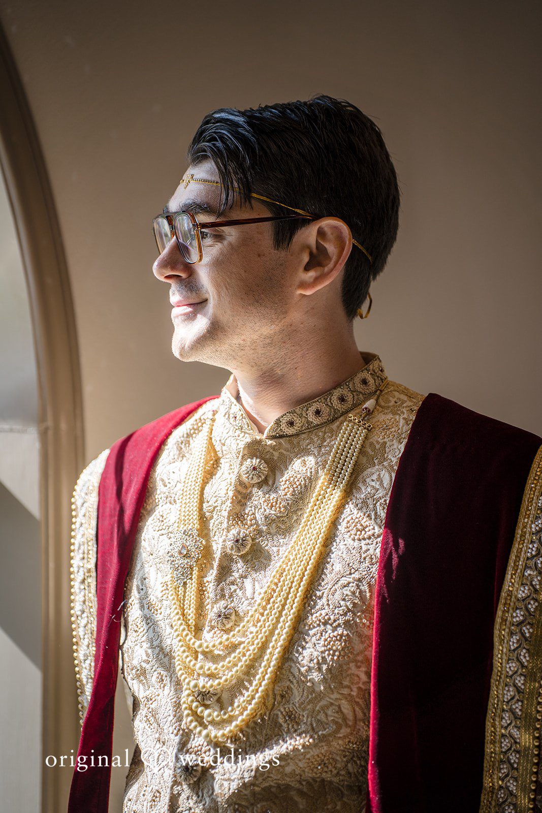 Nicholas + Nisha Groom wearing traditional attire and elaborate gold necklaces looking off to the side.