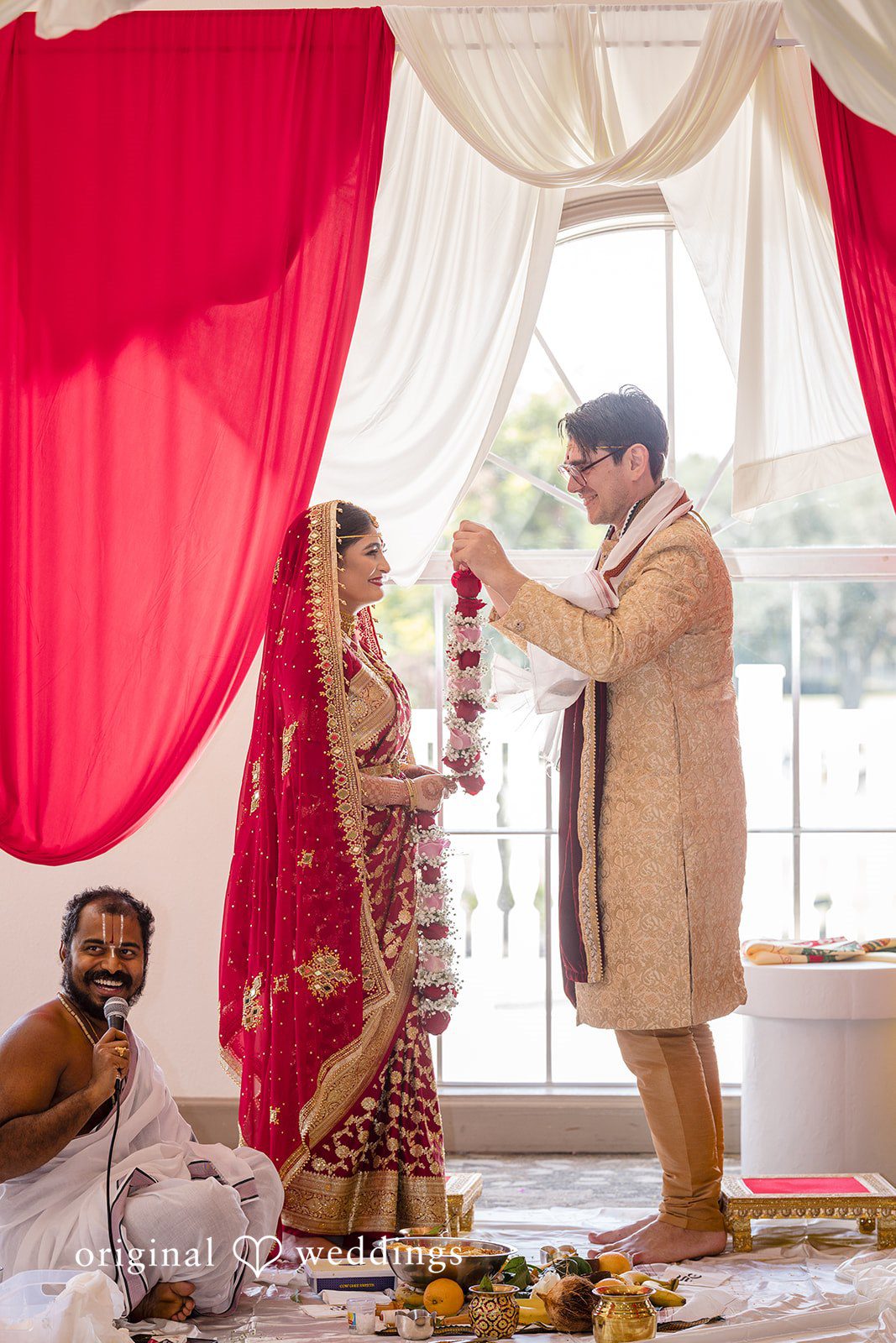 Nicholas + Nisha Groom standing near a red curtain during a traditional ceremony.