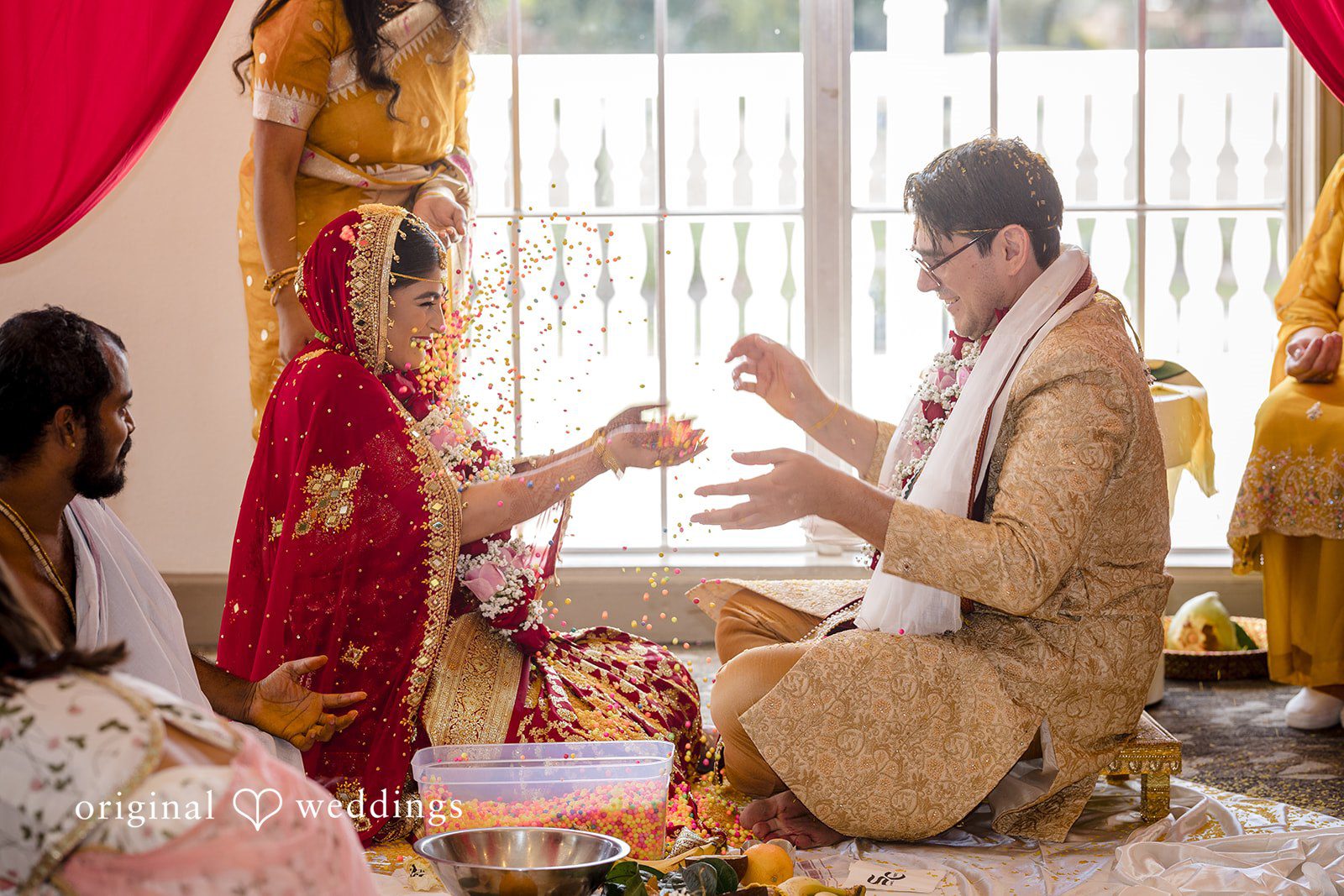 Nicholas + Nisha Bride and groom participating in a traditional ceremony near large windows.