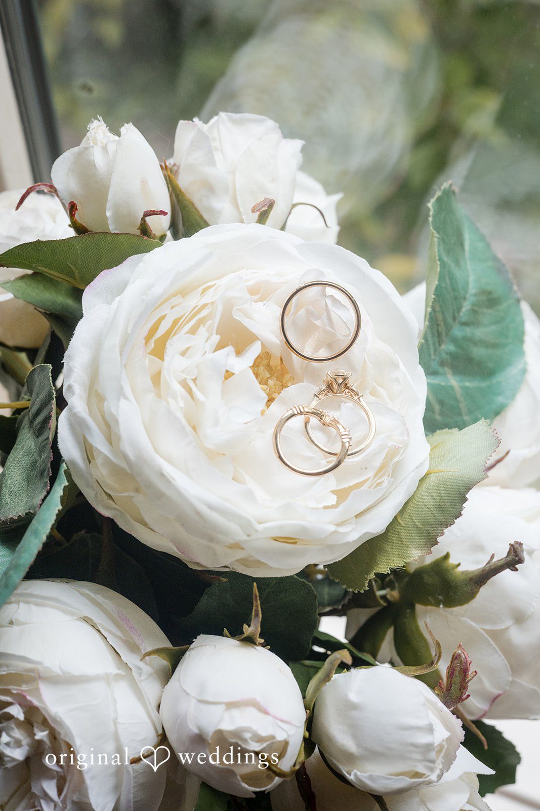 Macy + Nolan A close-up of a white flower bouquet featuring two wedding bands resting on the petals.