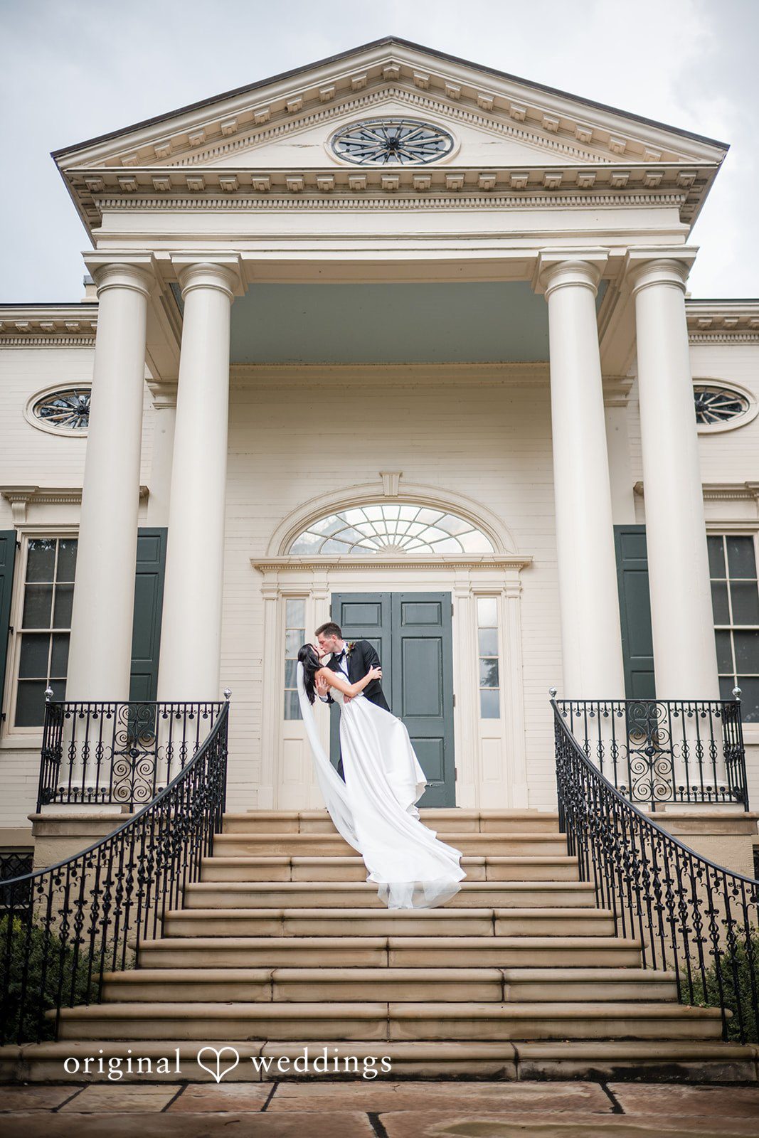 Macy + Nolan A bride and groom standing on the steps of a large historic estate with columns.