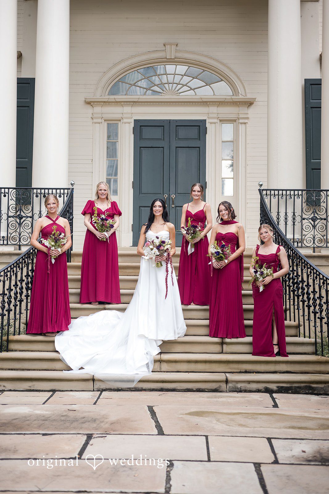 Macy + Nolan Bridesmaids in burgundy dresses standing on the steps of a building with the bride.