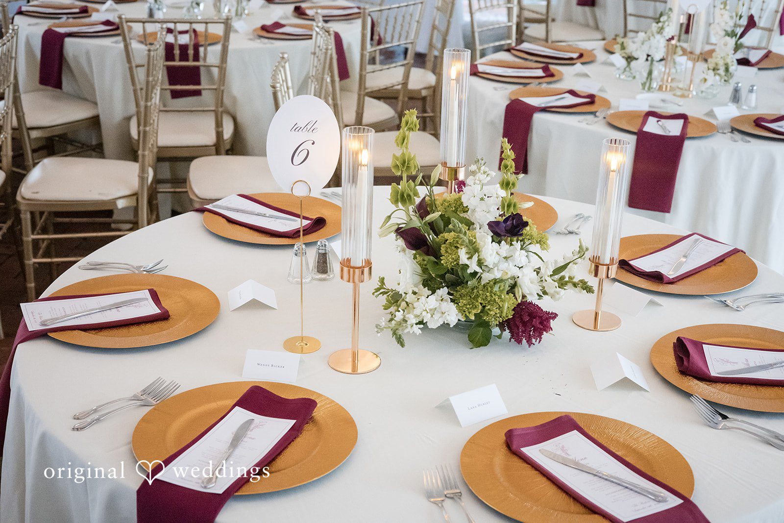 Macy + Nolan A decorated round reception table featuring white floral centerpieces and burgundy napkins.