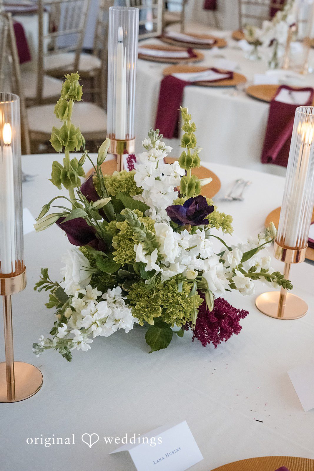 Macy + Nolan A close-up view of a dining table decorated with green vines and white flowers.