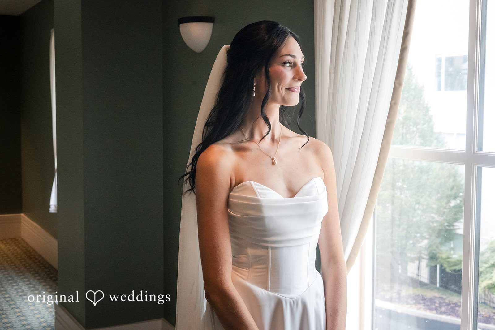 Macy + Nolan A bride in a white gown looking out a large window.