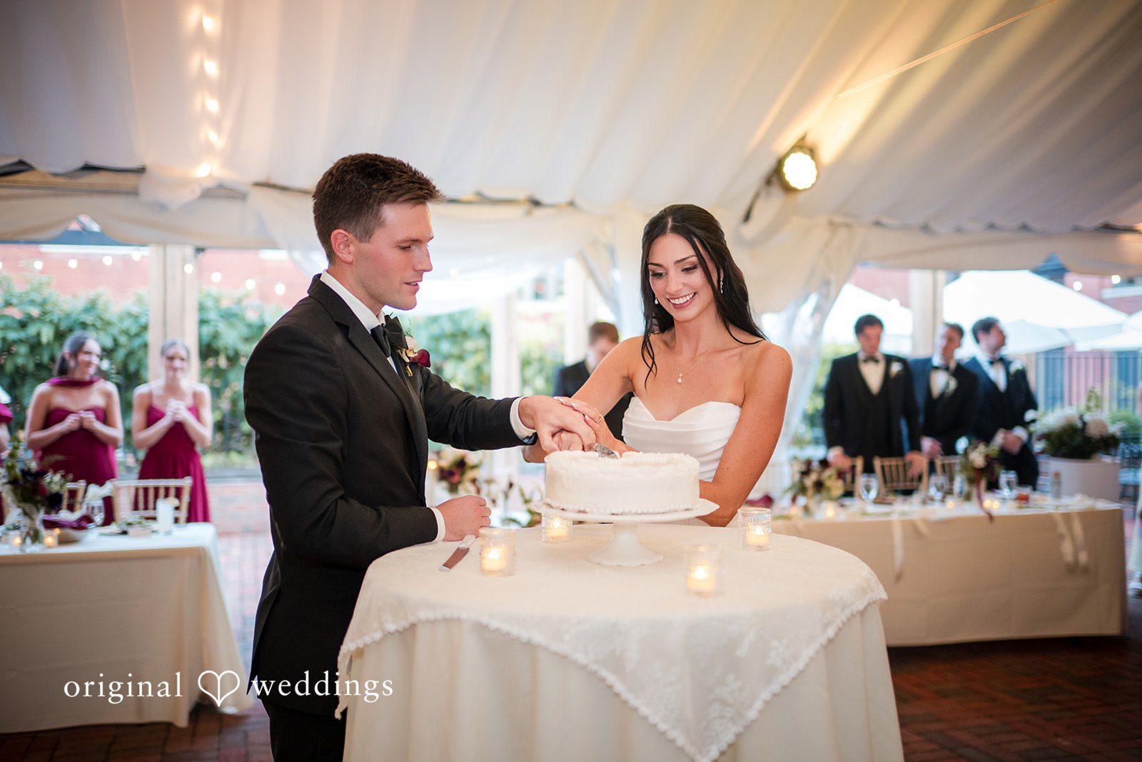 Macy + Nolan A bride and groom cutting their multi-tiered white wedding cake together.