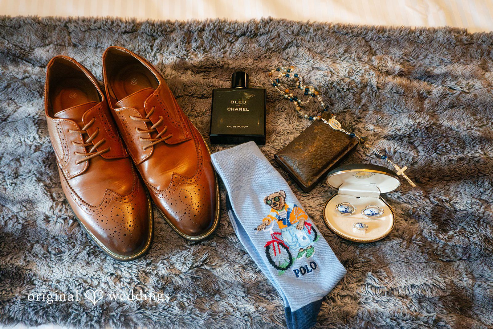Selena + Ezequiel A flat lay display of groom details including brown leather shoes, a tie, and accessories.