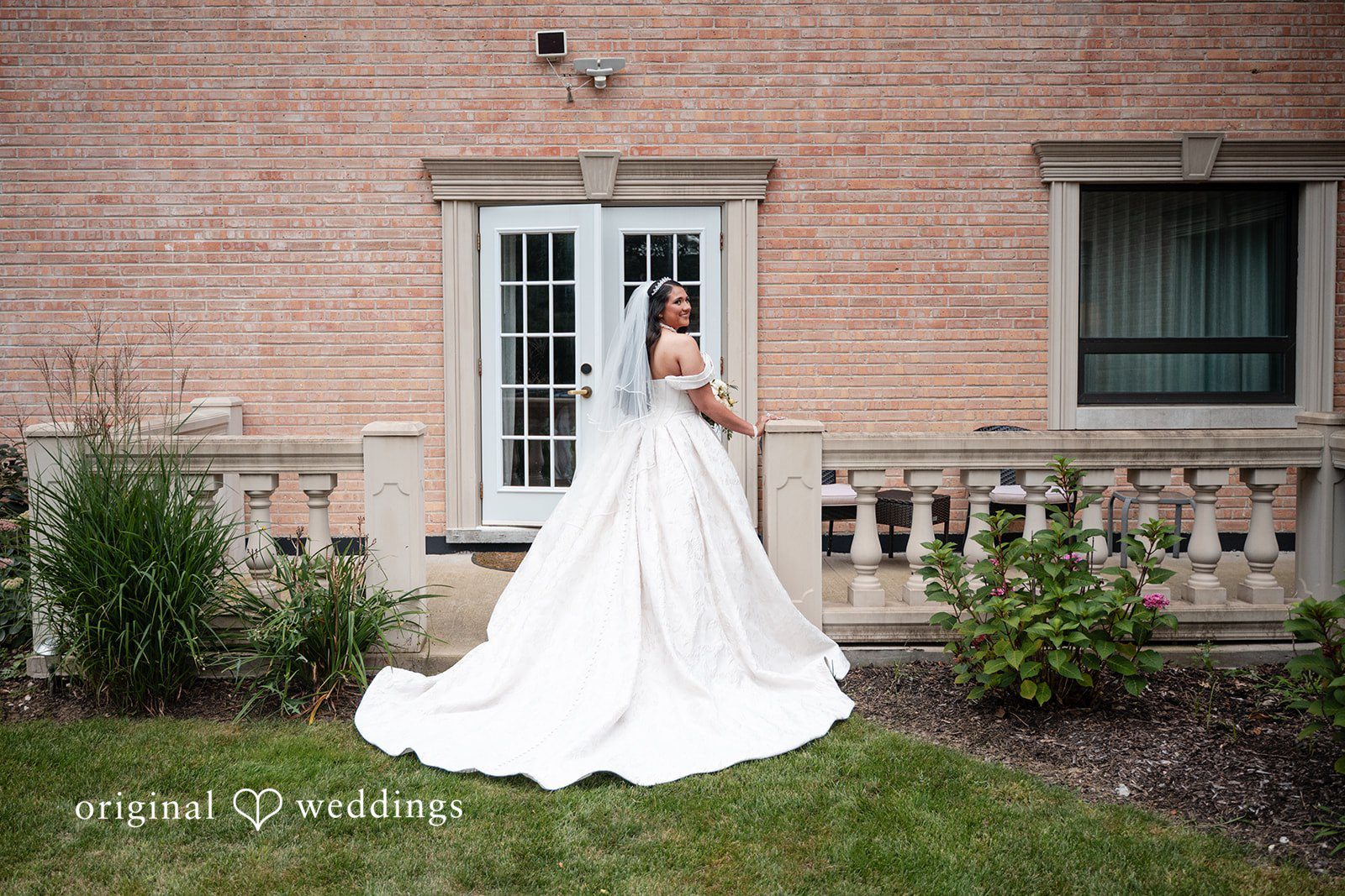 Selena + Ezequiel A bride in a white dress stands outside posing next to a large building wall.
