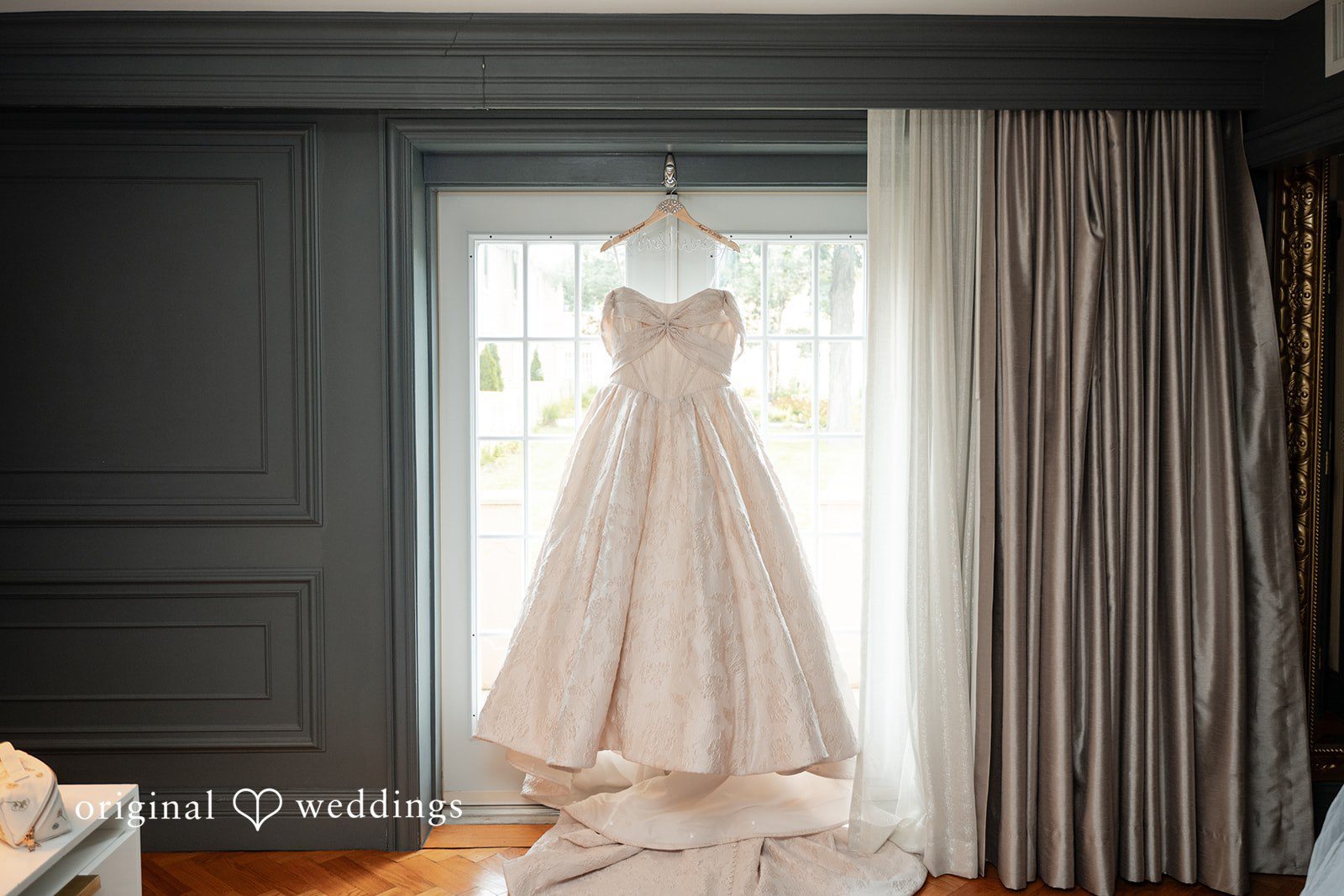 Selena + Ezequiel A white wedding dress hangs vertically on a display stand in front of curtains.
