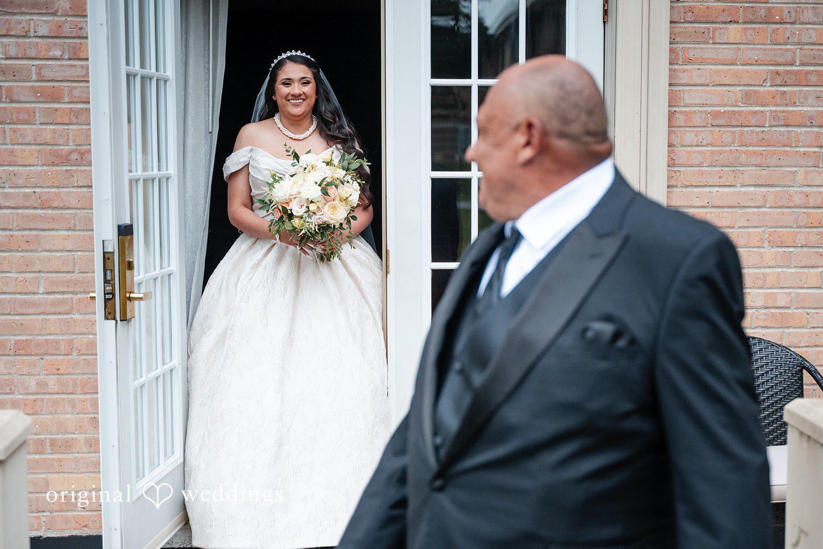 Selena + Ezequiel A man in a dark suit stands looking toward a doorway where a bride is partially visible.
