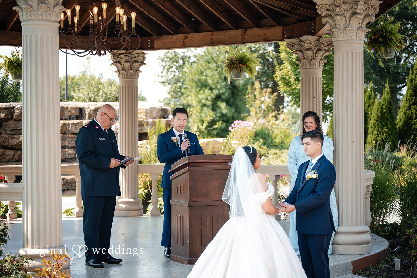 Selena + Ezequiel A bride stands facing an officiant and guests at an altar during a wedding ceremony.