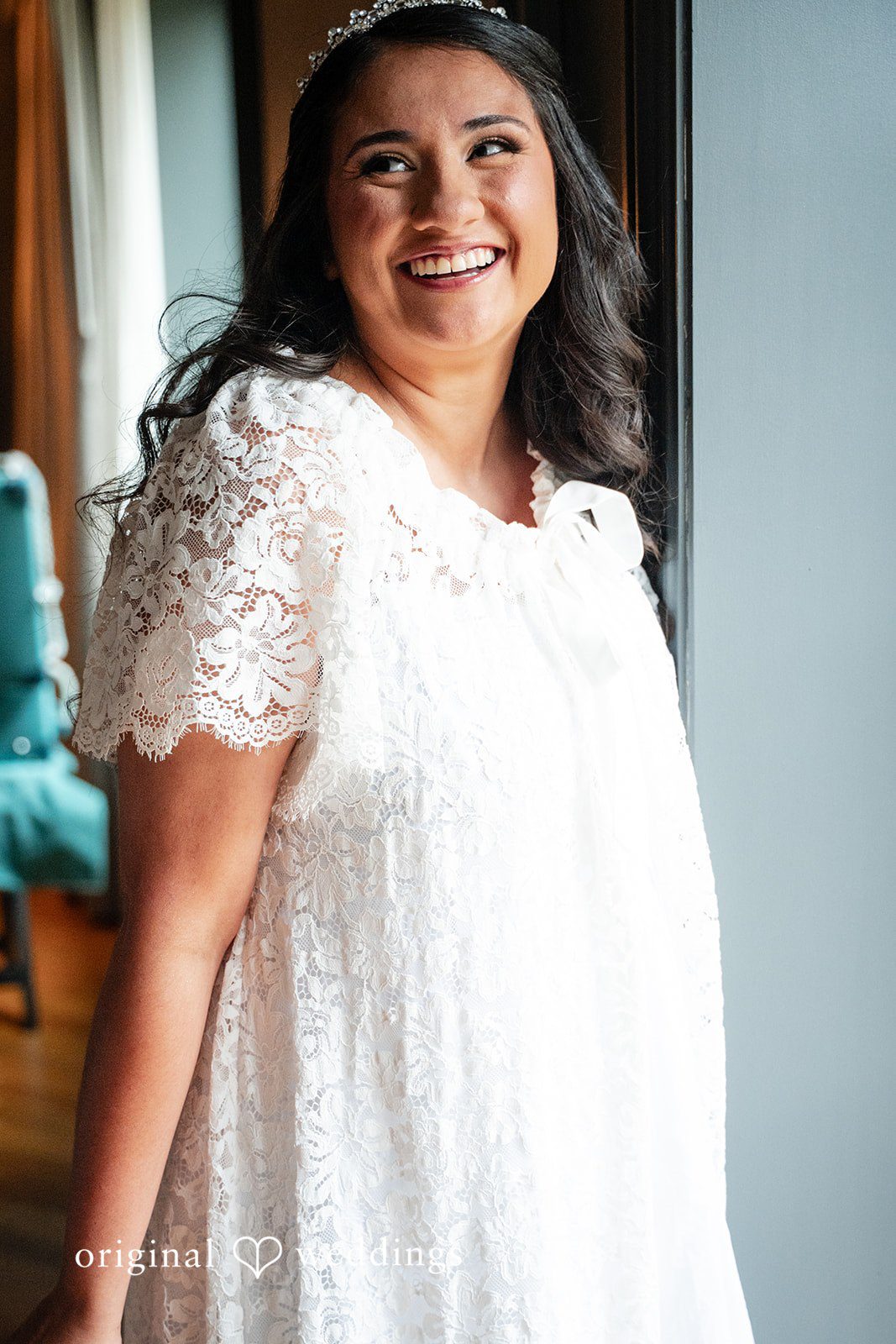 Selena + Ezequiel A candid shot of a smiling woman looking to the side in a white lace garment.