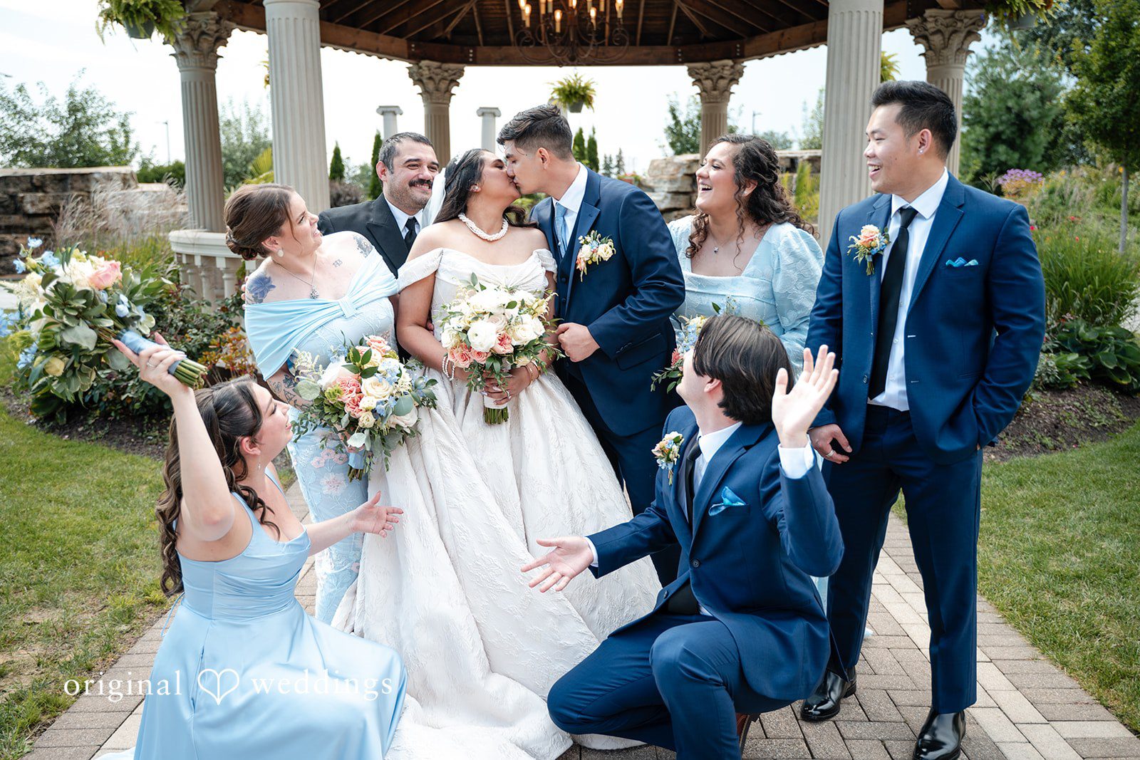Selena + Ezequiel A group of bridesmaids in light-blue dresses surround a bride and groom on a path.