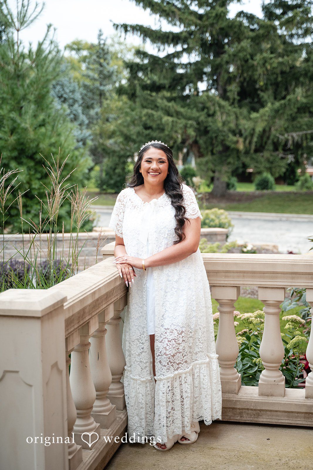 Selena + Ezequiel A bride in a white wedding gown poses smiling on a stone terrace.