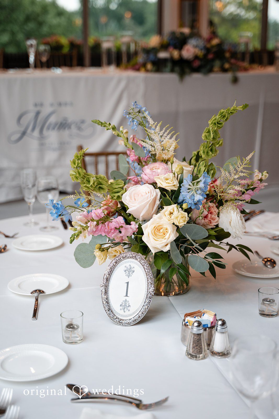 Selena + Ezequiel A floral centerpiece featuring pastel roses and green foliage on a reception table.