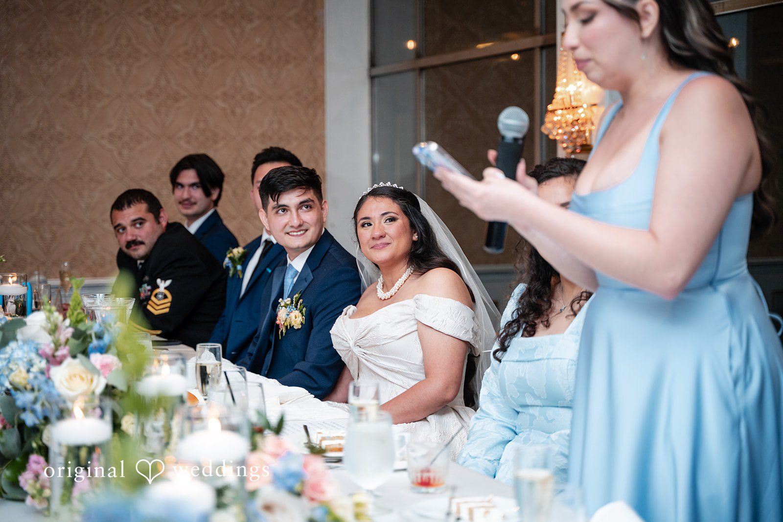 Selena + Ezequiel A bridesmaid in a light-blue dress stands using a microphone to deliver a toast at the head table.