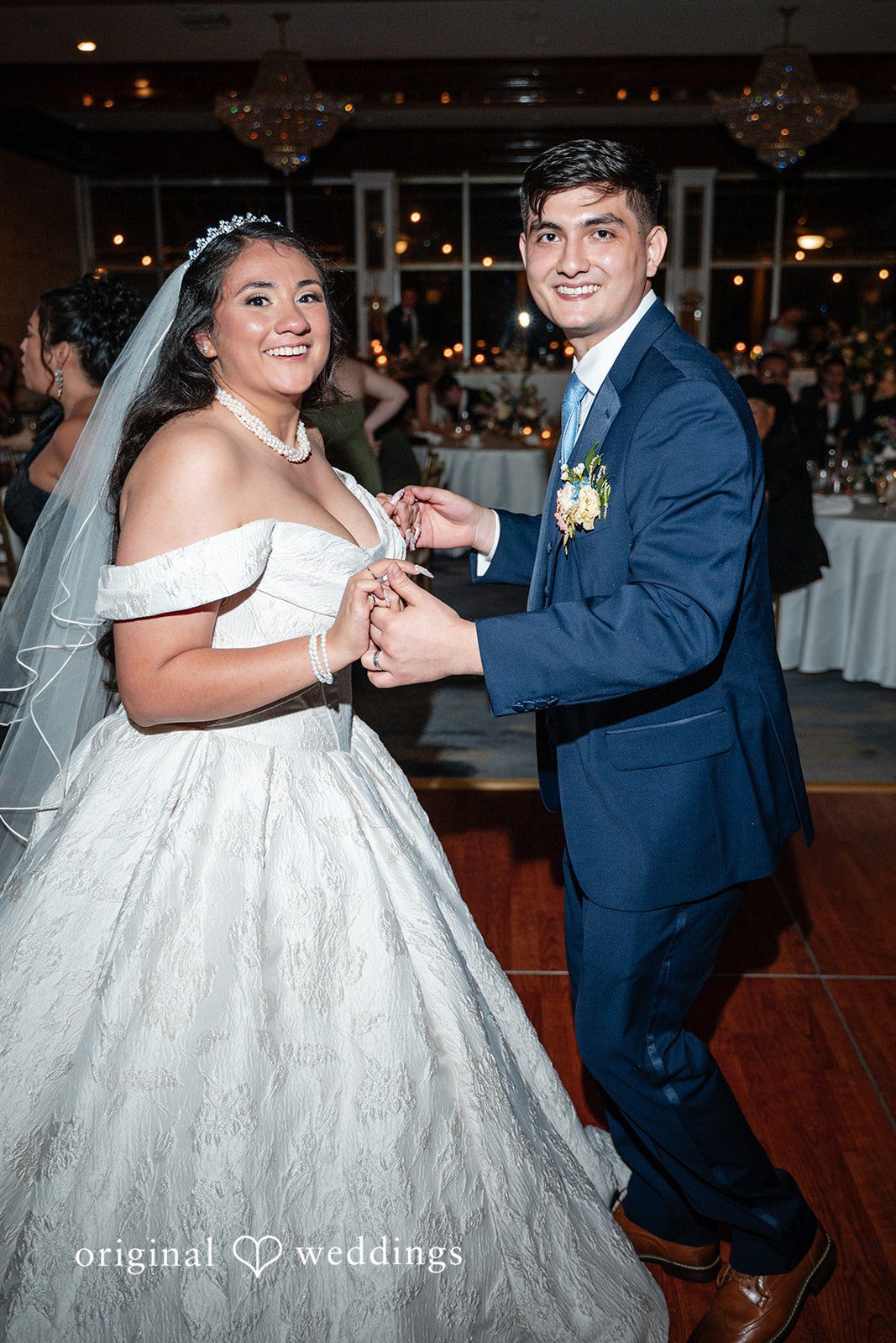 Selena + Ezequiel A bride and groom hold hands while smiling and dancing together on a dance floor.