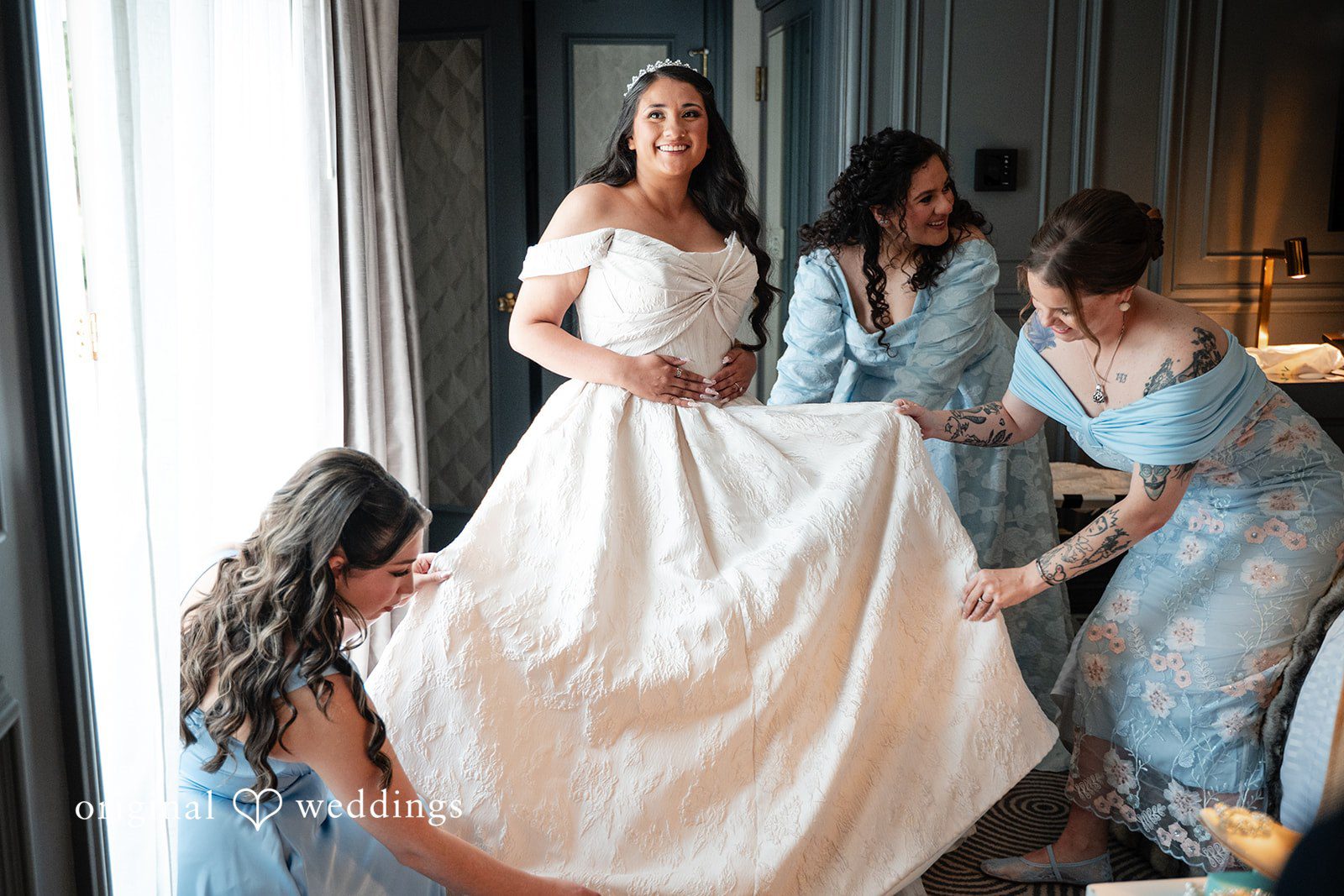 Selena + Ezequiel A bride in a white gown stands as bridesmaids assist her with her dress adjustments.