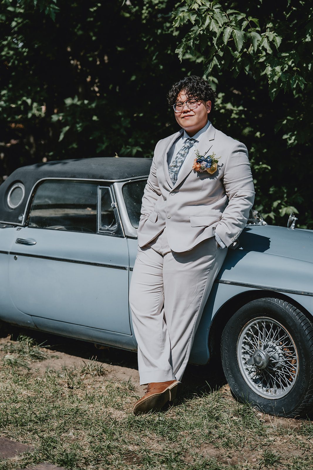 Partner in a light suit leaning on a vintage car at The Lyons Farmette