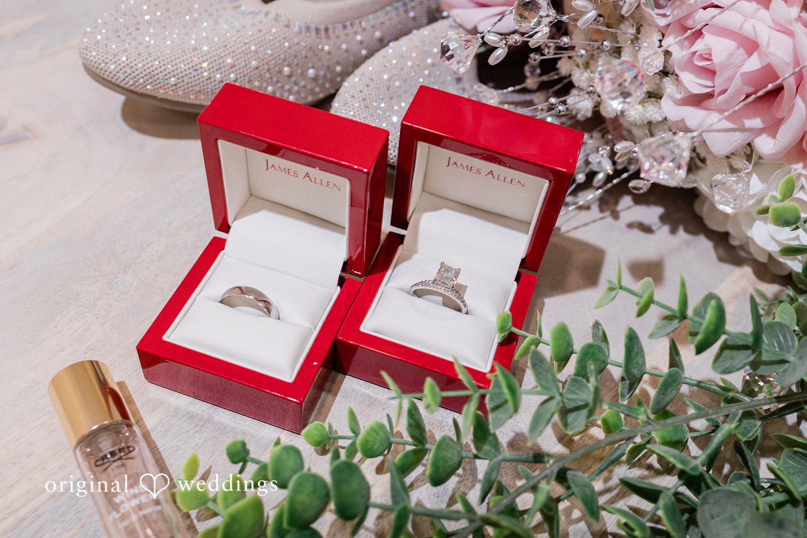 Daniel + Dalte Two red velvet jewelry boxes containing wedding rings placed amidst greenery.