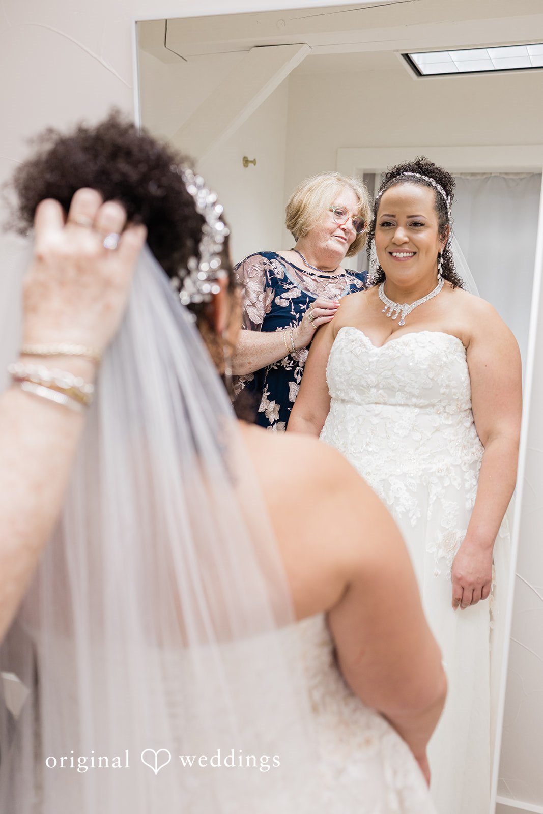 Daniel + Dalte A bride adjusts her veil while standing with bridesmaids in a dressing area.