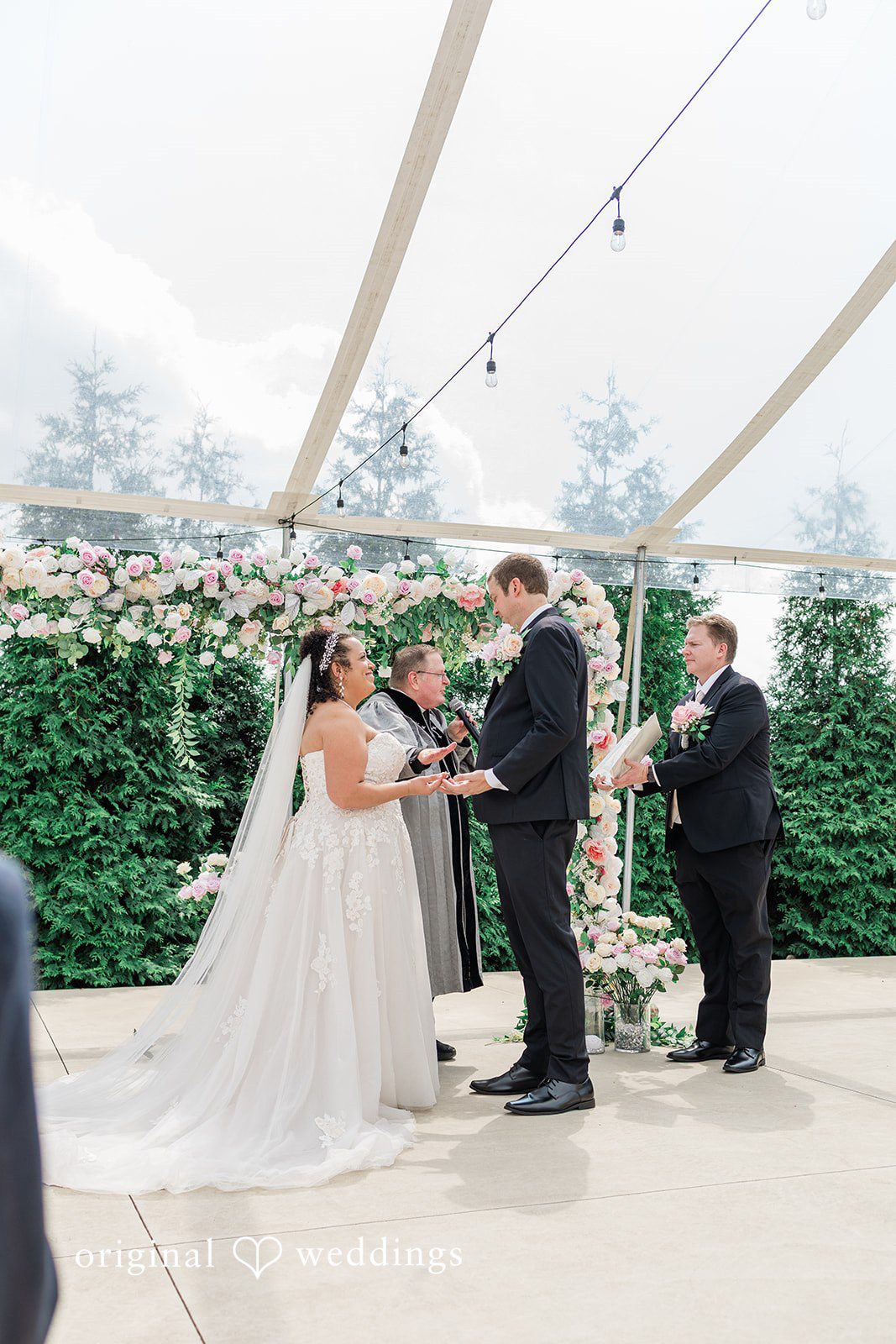 Daniel + Dalte A bride and groom exchange vows under a canopy with guests watching from the side.