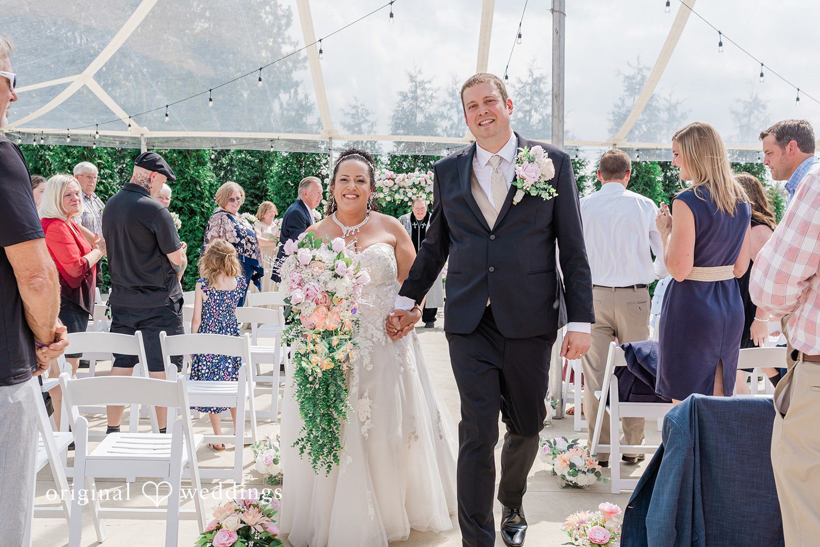 Daniel + Dalte A newlywed bride and groom walk down the aisle together as guests look on.