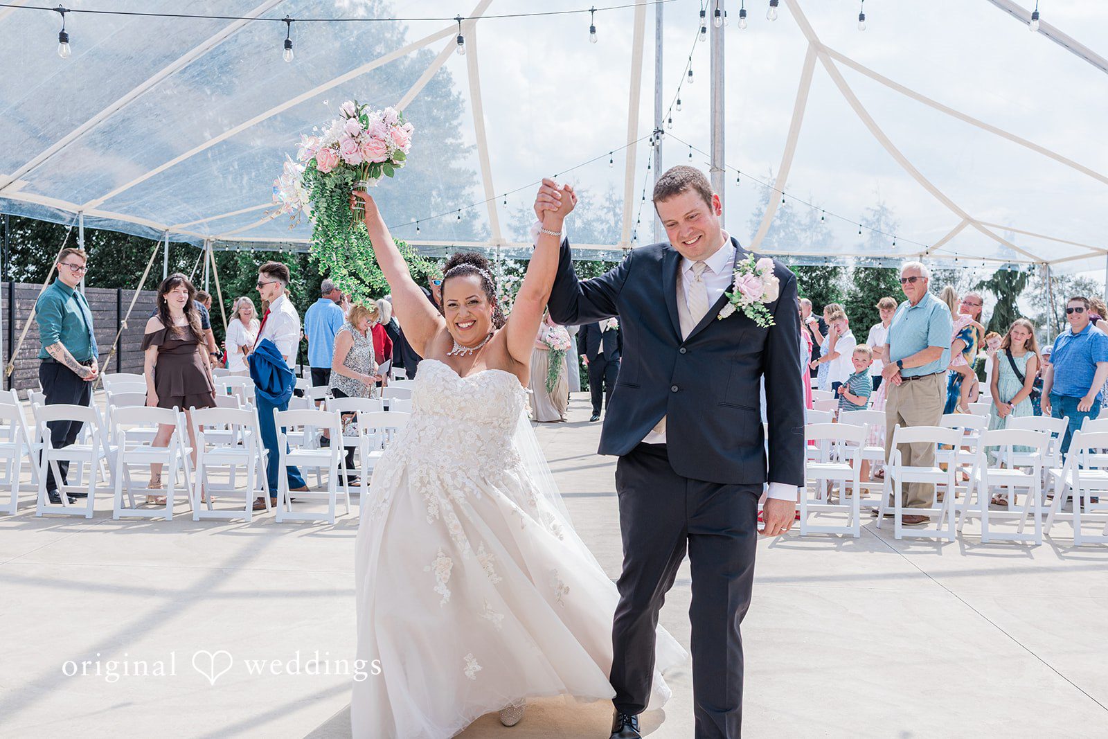 Daniel + Dalte A bride and groom raise their hands in celebration while walking down the aisle after their ceremony.