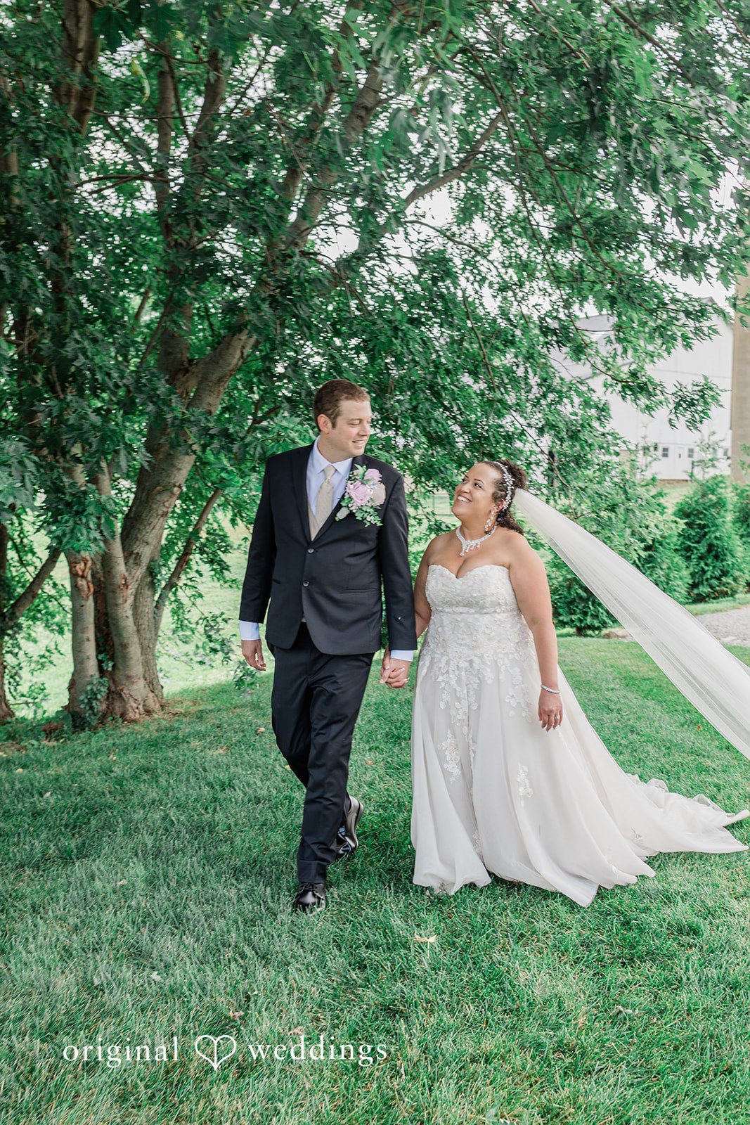 Daniel + Dalte A bride and groom holding hands while walking across a green grassy field.