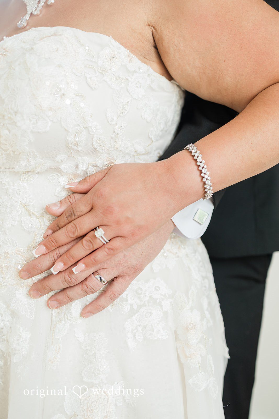 Daniel + Dalte A close-up of a bride's hand, displaying a wedding ring, resting on her white gown.